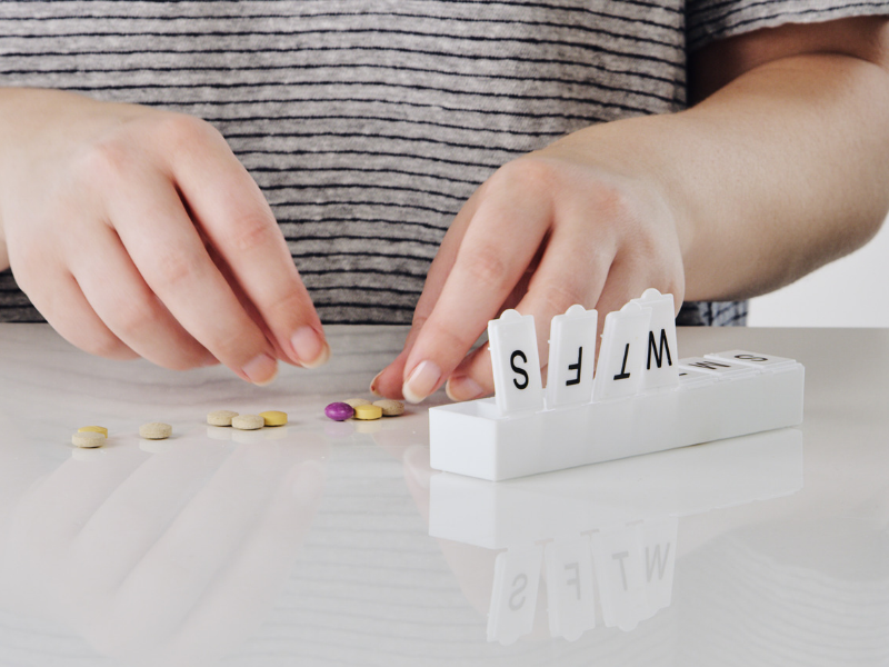 A person organising tablets in a weekly medicine box.