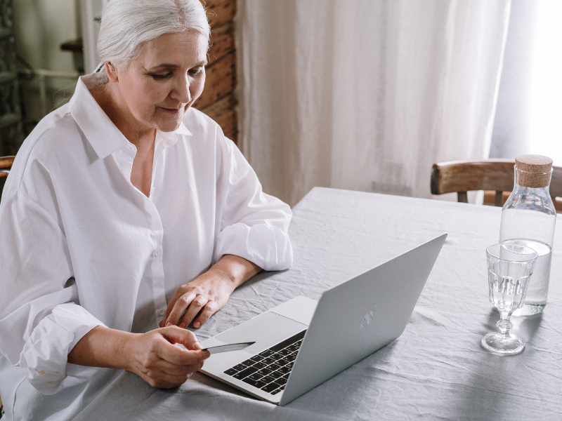 An older woman using a laptop and holding a bank card.